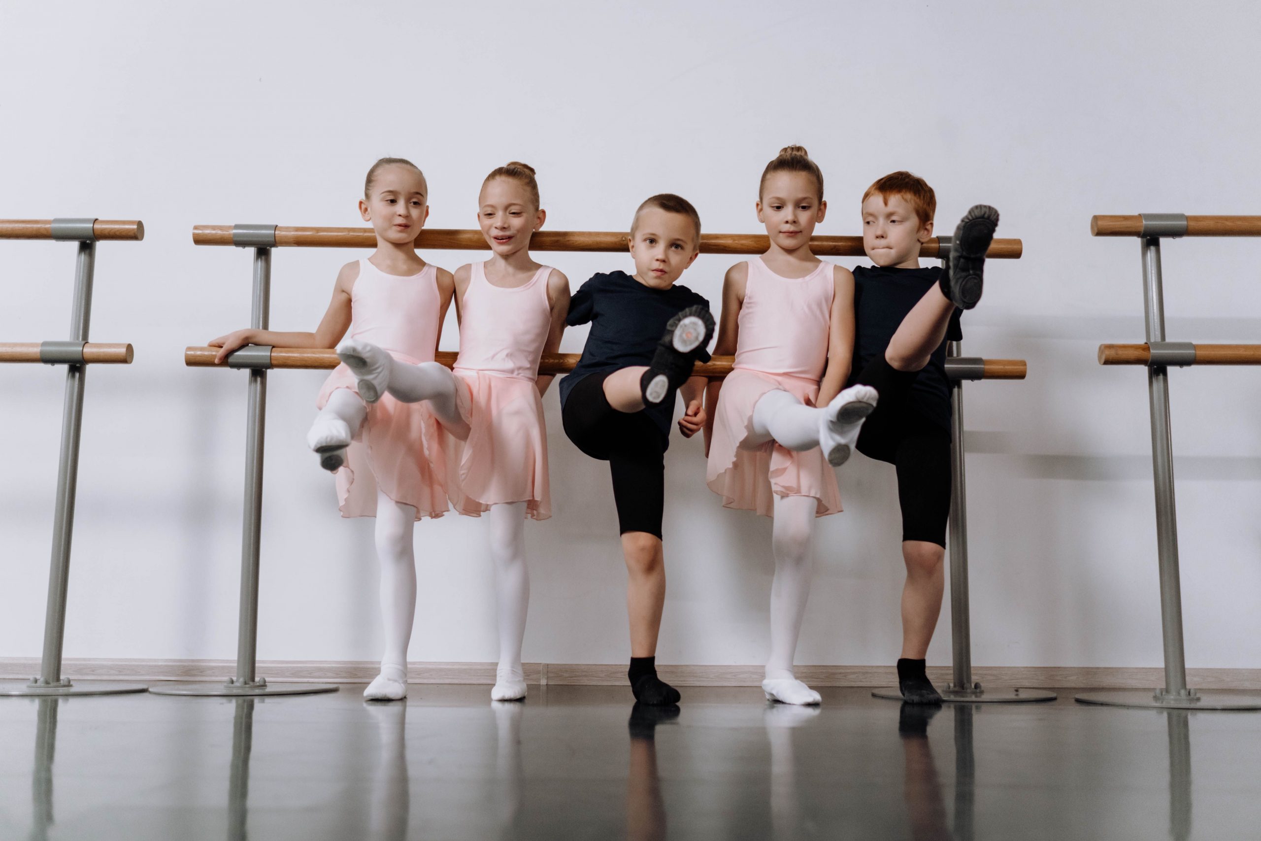 Children having fun practicing ballet at the barre with big smiles in a studio setting.