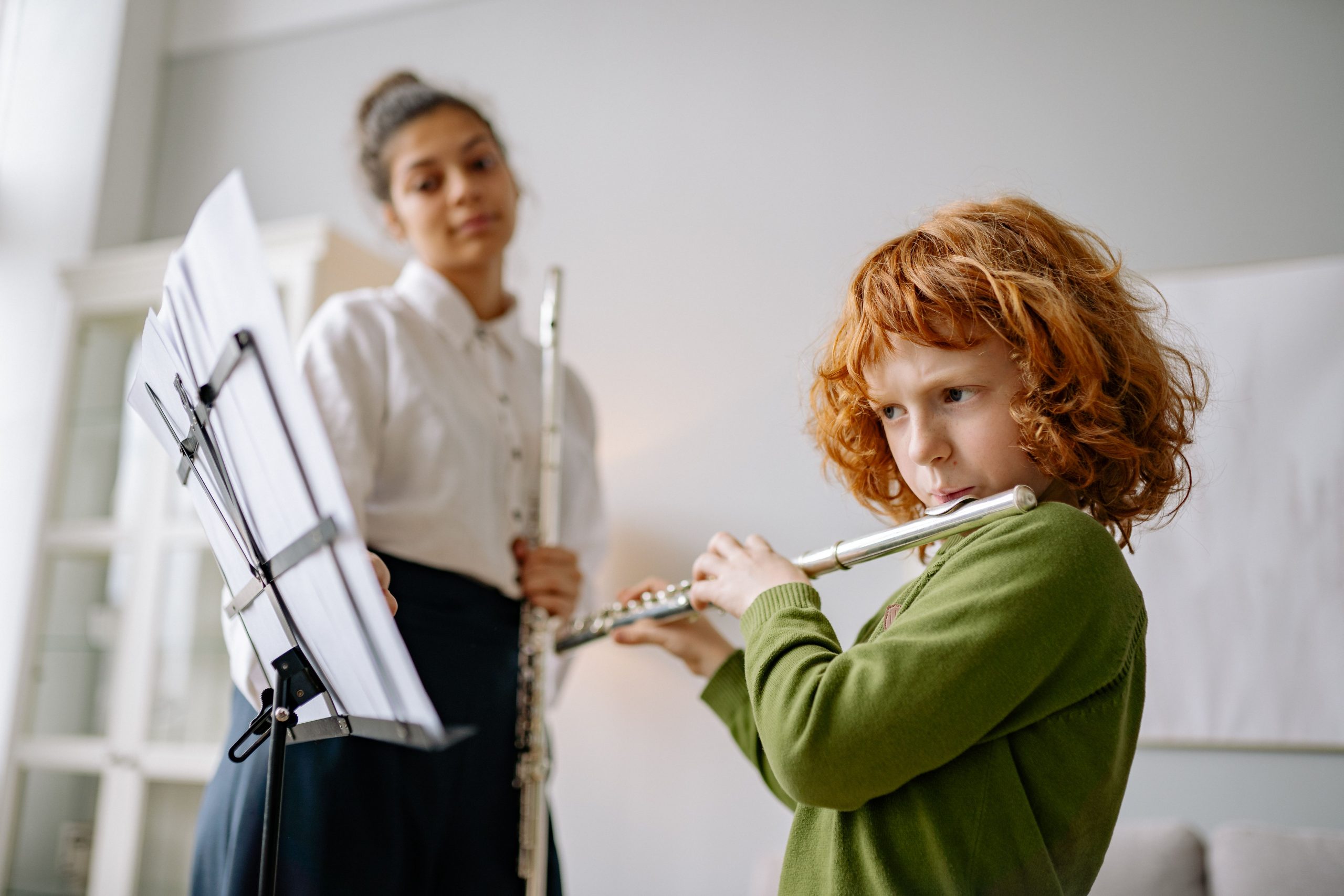 A young boy learning flute with a female teacher at home, focused on music practice.